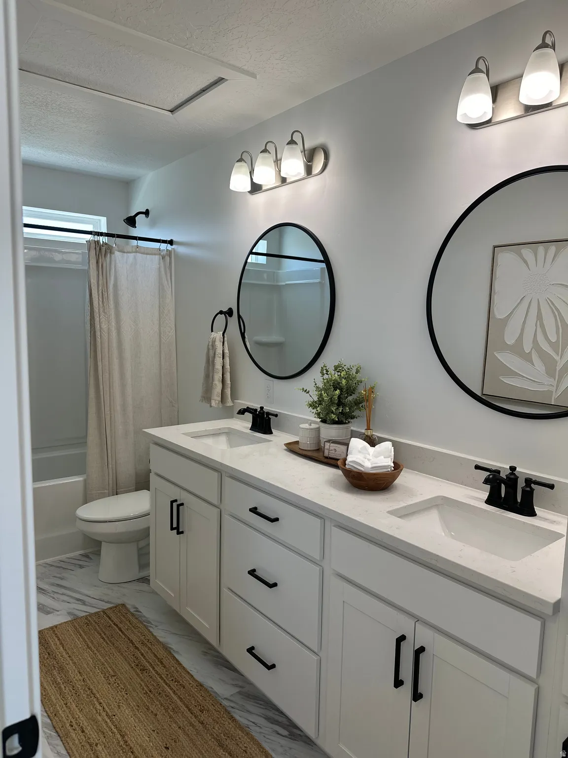 Full bathroom featuring double vanity, a textured ceiling, shower / bathtub combination with curtain, and light marble finish floors