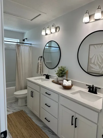 Full bathroom featuring double vanity, a textured ceiling, shower / bathtub combination with curtain, and light marble finish floors