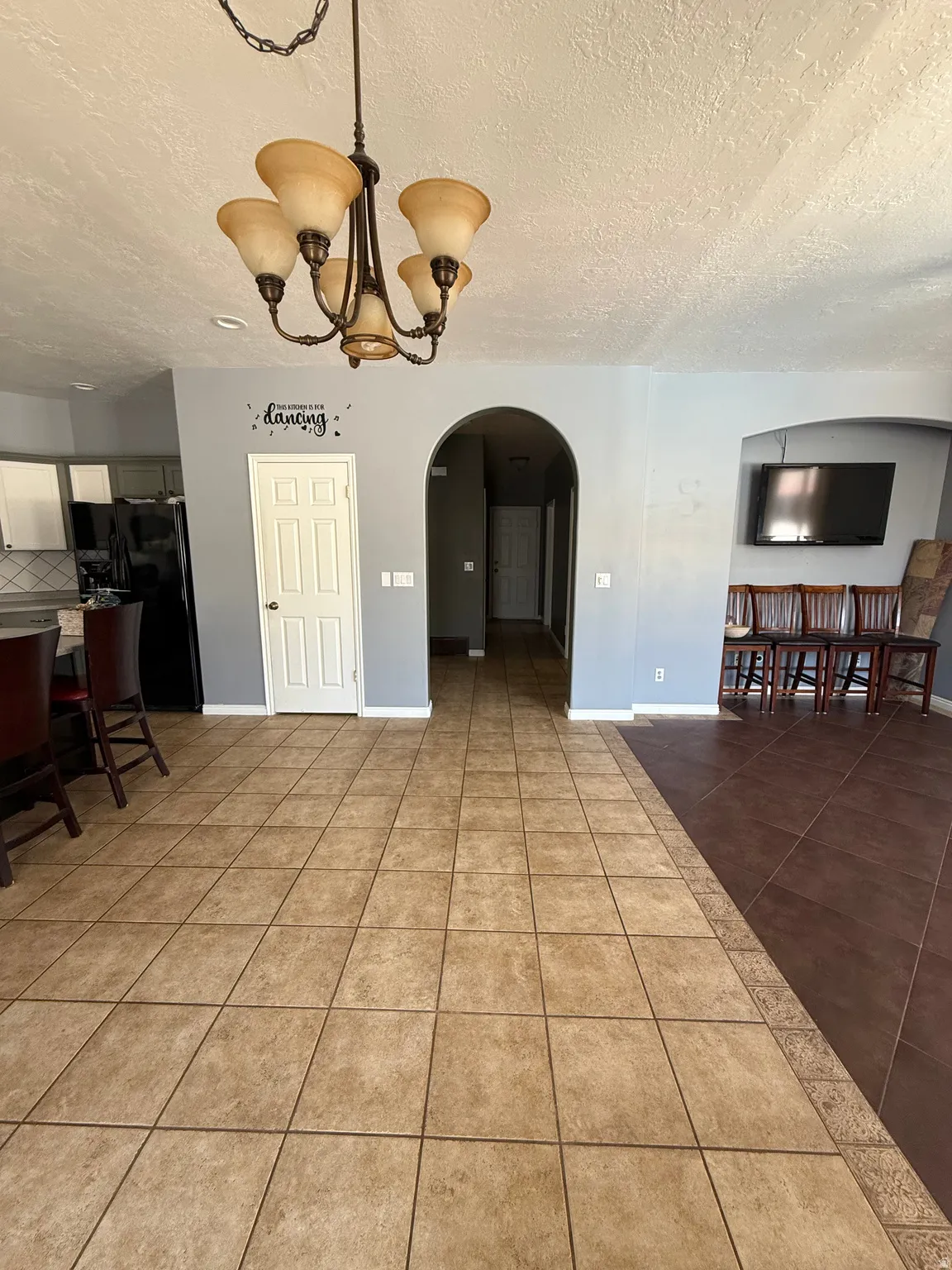 Open-concept living space featuring a central chandelier, arched doorways, and a combination of light and dark ceramic tile flooring