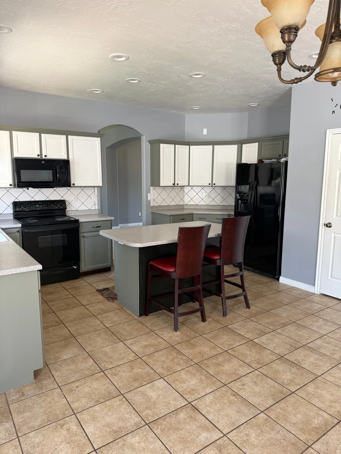 Spacious kitchen featuring an island with countertop seating, tile flooring, recessed lighting, two-tone cabinetry with black hardware, and an arched doorway