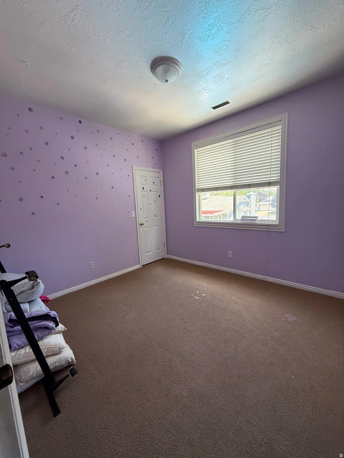Carpeted room featuring a ceiling-mounted light fixture, a window with blinds, and a white door with a brass-finish handle