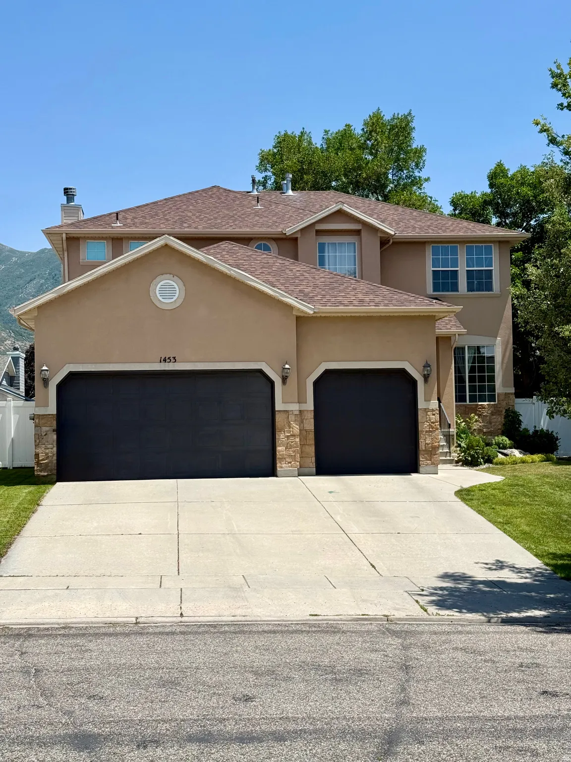 Stucco exterior featuring a dual garage with dark doors, stone accents, and a concrete driveway