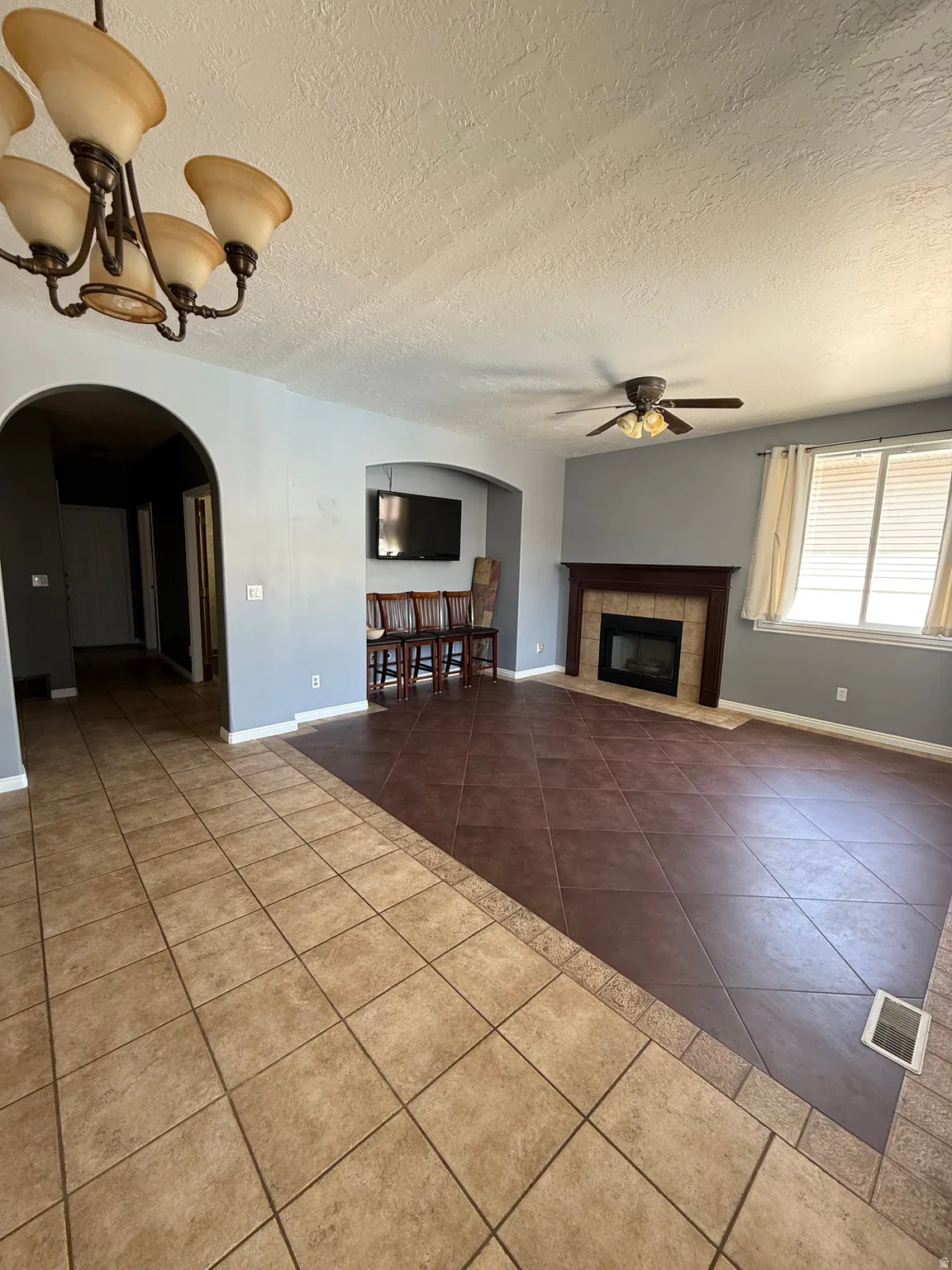 Spacious living area featuring a tile floor with a contrasting border, an arched entry, and a built-in fireplace with a dark wood mantel