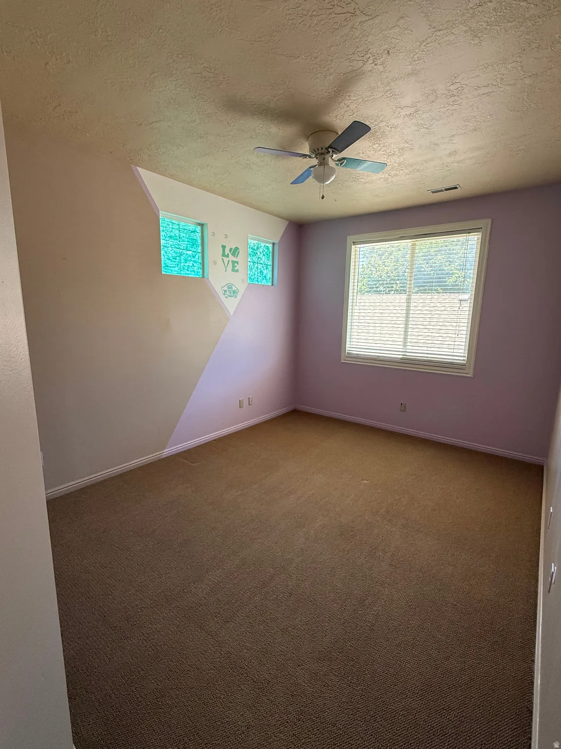 Spacious room featuring broadloom carpet, multiple windows with natural light, a ceiling fan, and baseboard trim