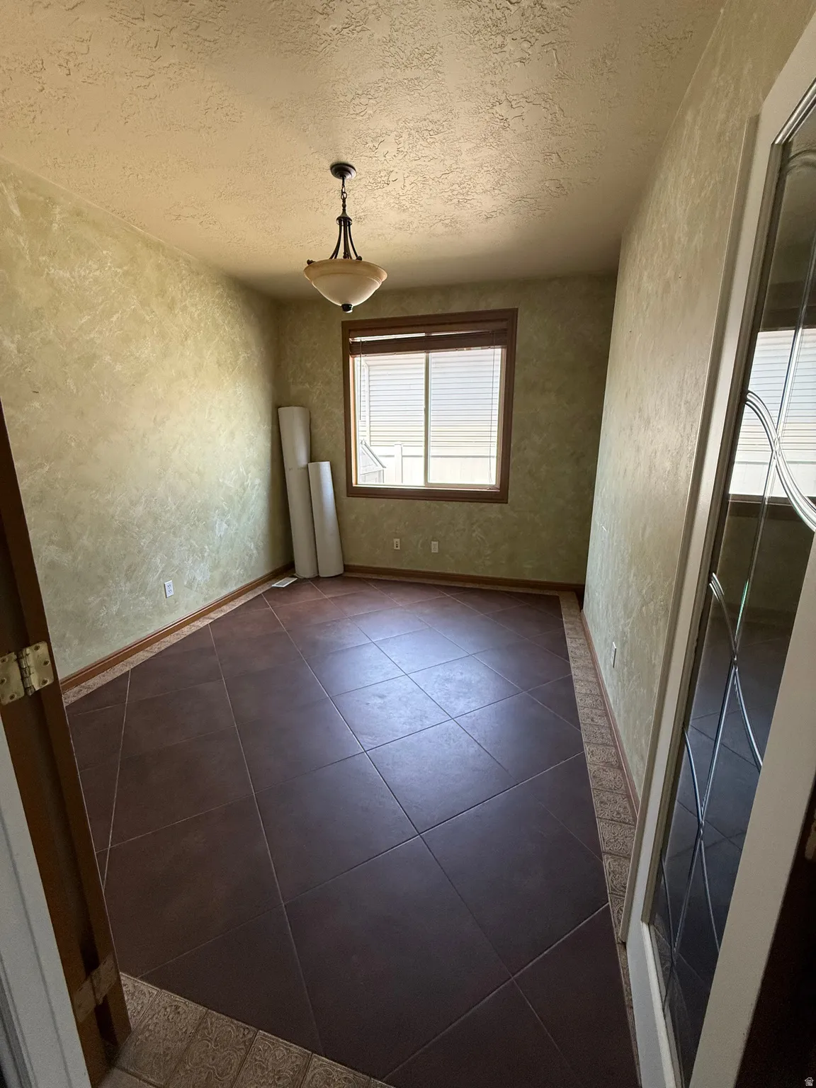Room featuring large format brown floor tiles with diagonal accents, textured green walls, and a multi-pane window with wood-finish trim