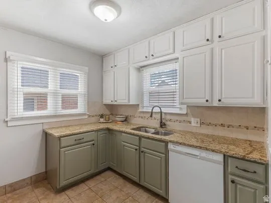Kitchen featuring dishwasher, light stone countertops, white cabinets, and backsplash
