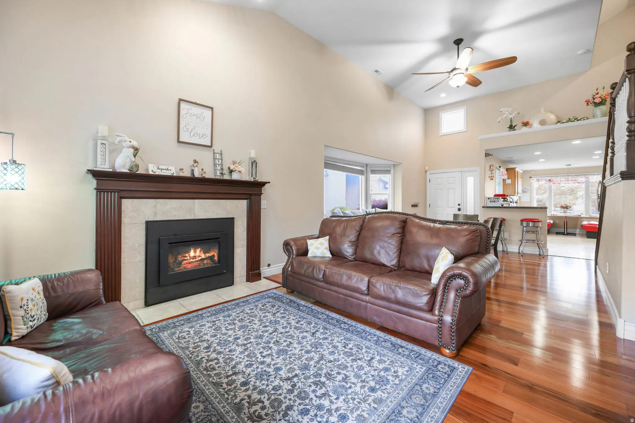 Living area with wood-type flooring, ceiling fan, plenty of natural light, a tiled fireplace, and a high ceiling