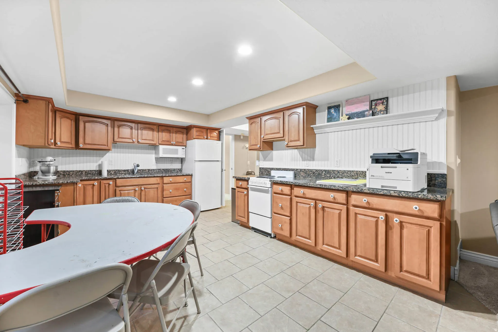 Kitchen featuring wood finish cabinetry, white appliances, dark stone countertops, wallpapered walls, and recessed lighting