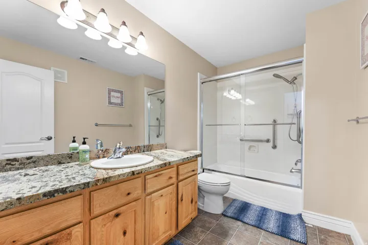 Full bathroom featuring vanity, bath / shower combo with glass door, and dark tile patterned flooring