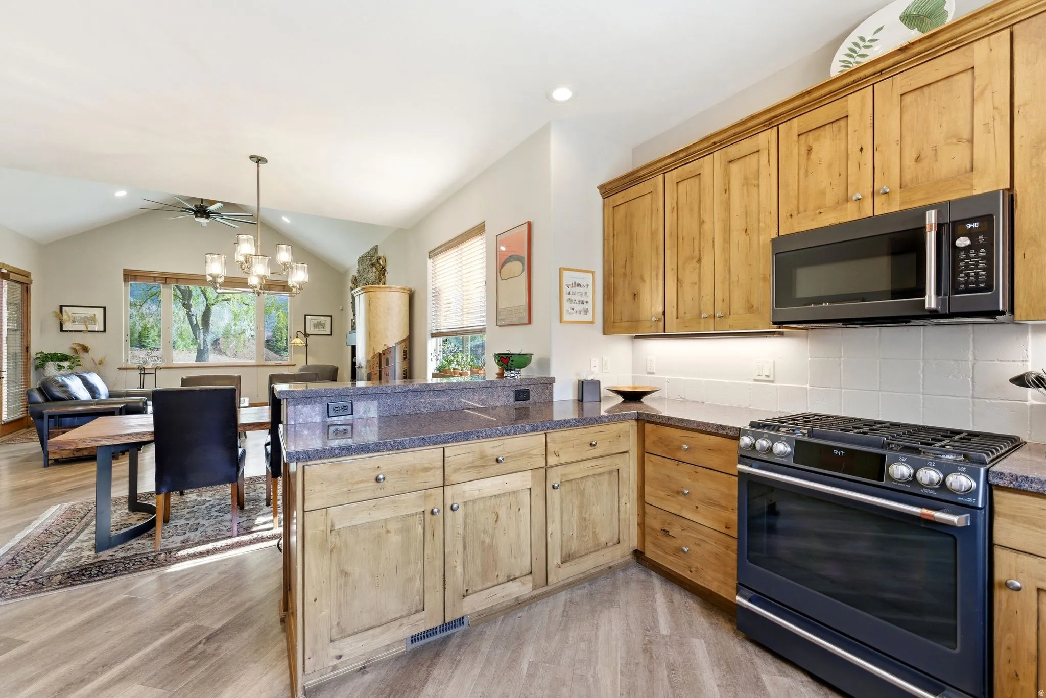 Kitchen with gas range, a peninsula, light wood-style flooring, tasteful backsplash, and lofted ceiling