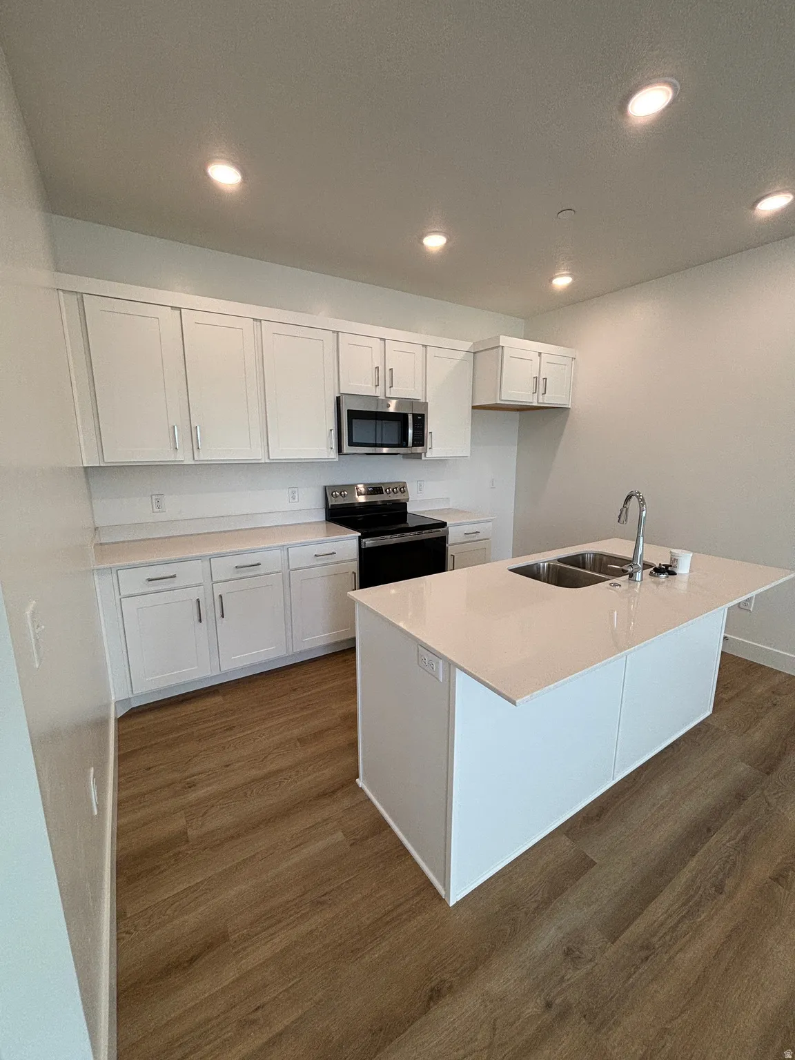 Kitchen with white cabinetry, stainless steel appliances, dark wood-type flooring, an island with sink, and recessed lighting