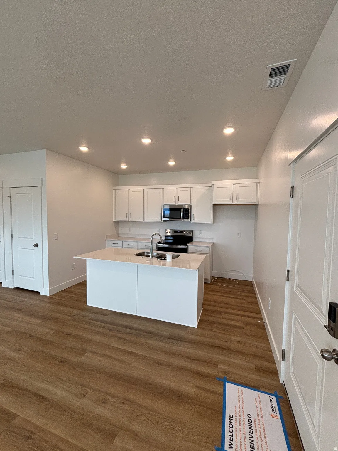 Kitchen with white cabinets, dark wood-style flooring, stainless steel appliances, a center island with sink, and recessed lighting