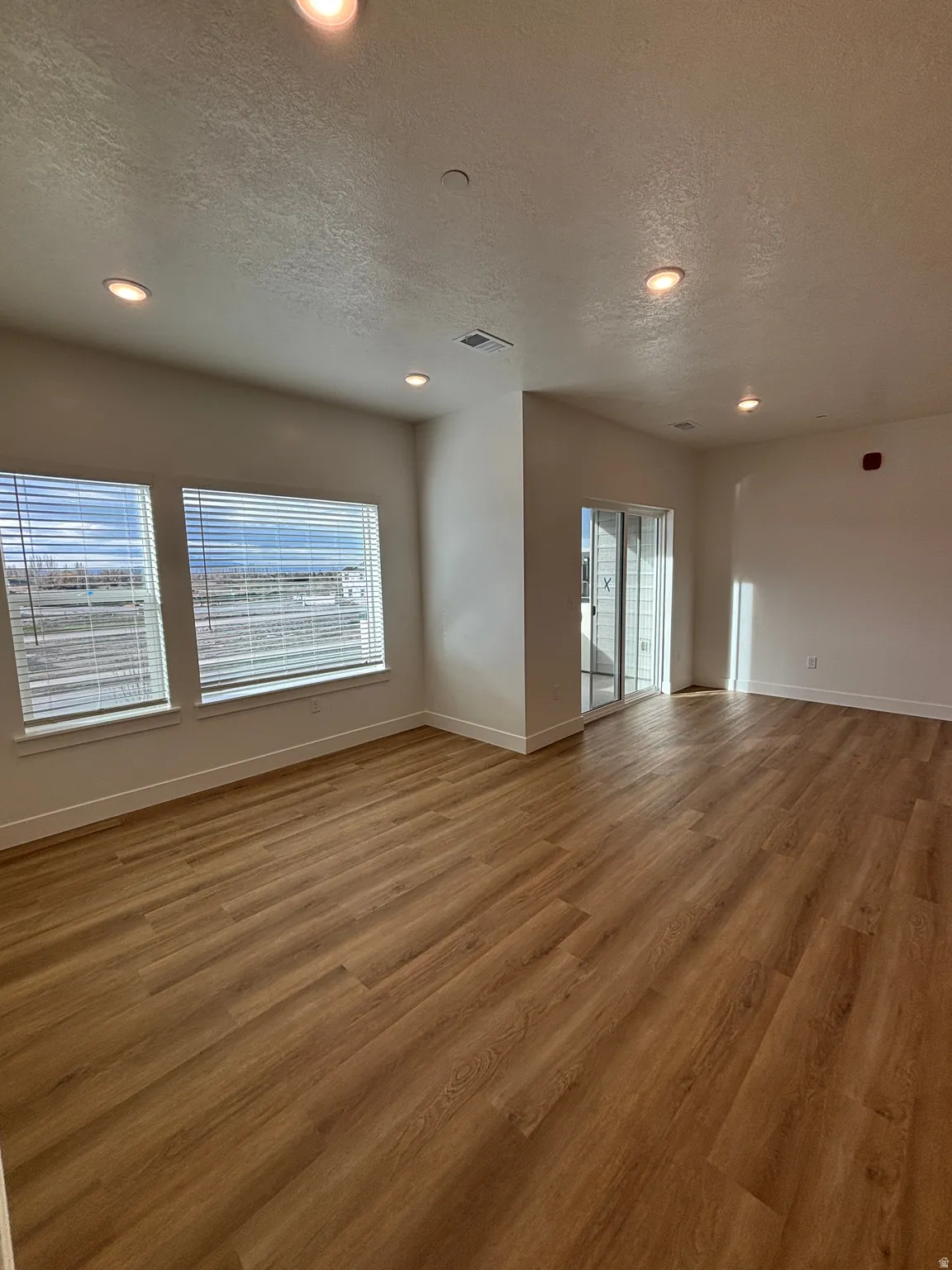 Unfurnished living room with a textured ceiling, recessed lighting, and wood finished floors