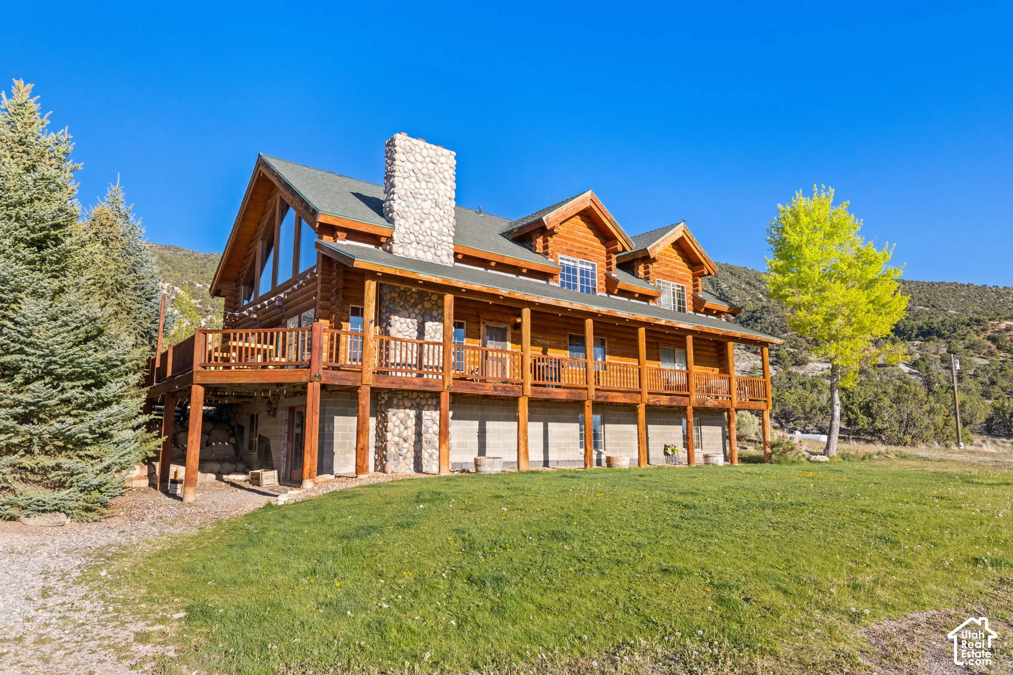 Front view of property featuring a yard, a chimney, log exterior, stone siding, and a large valley viewing wraparound porch