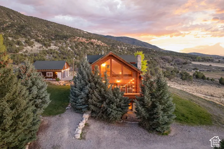 View of front of house with a mountain view, a chimney, log exterior, covered porch, and a lawn