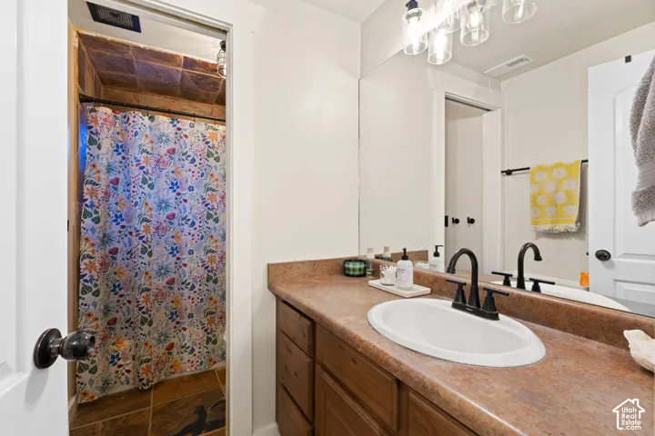 Full bath with vanity, a shower with shower curtain, and dark stone finish floors