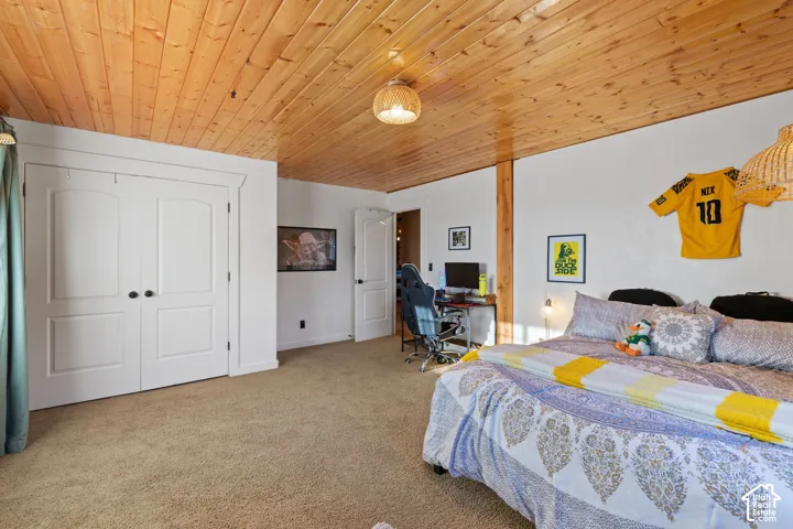 Carpeted bedroom featuring a desk, a closet, and wood ceiling