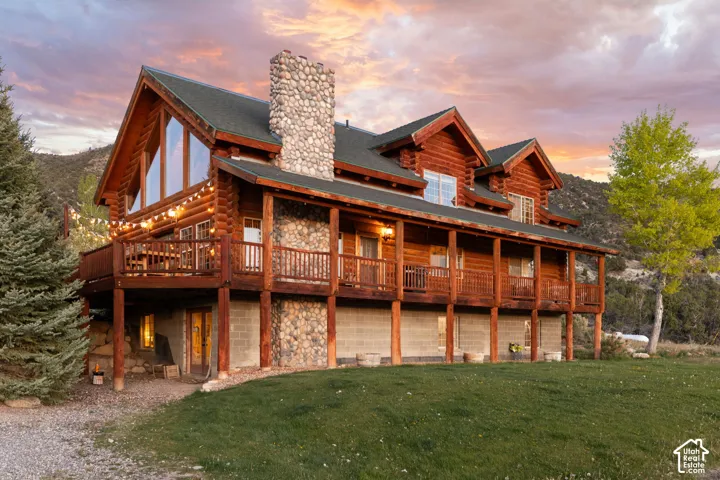 Front view of property featuring a yard, a chimney, log exterior, stone siding, and a large valley viewing wraparound porch