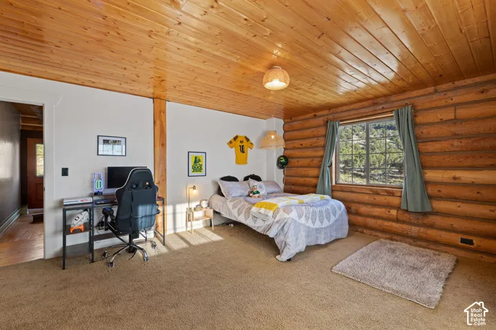 Bedroom featuring carpet flooring, wooden ceiling, log walls, and an office area