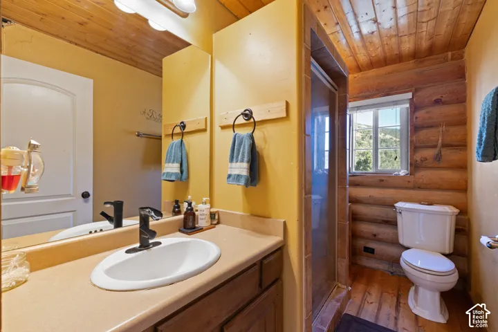 Bathroom featuring wooden ceiling, vanity, a stall shower, log walls, and wood-type flooring