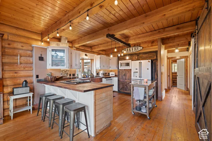 Kitchen with wood counters, a barn door, light wood finished floors, a peninsula, and a breakfast bar
