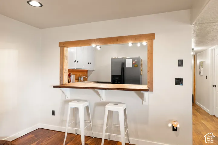 Kitchenette featuring a breakfast bar area, refrigerator with ice dispenser, white cabinets, dark wood finished floors, and recessed lighting