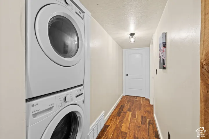 Laundry area featuring a textured ceiling, stacked washer / drying machine, and dark wood-type flooring