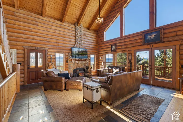 Living room with a high wood beamed ceiling, a fireplace, stone tile flooring, french doors, and rustic log walls