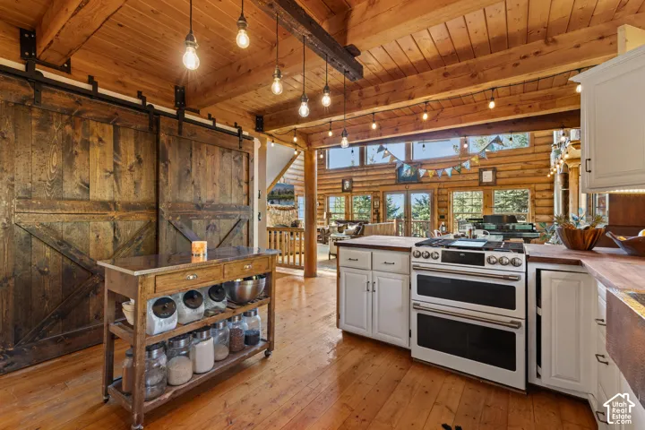 Kitchen featuring light wood finished floors, a wooden ceiling with exposed beams, a barn door, rustic walls, and double oven gas range