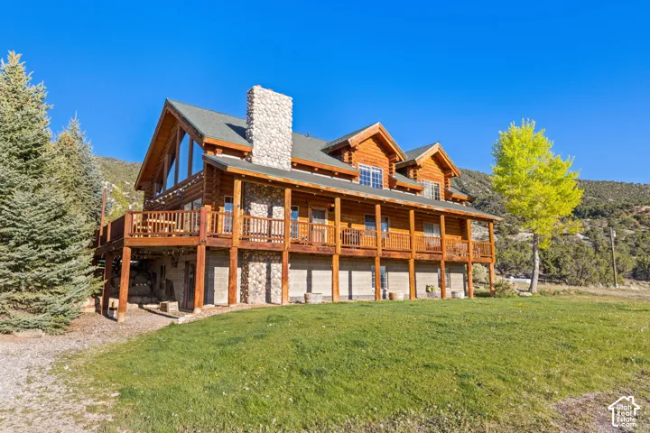 Front view of property featuring a yard, a chimney, log exterior, stone siding, and a large valley viewing wraparound porch