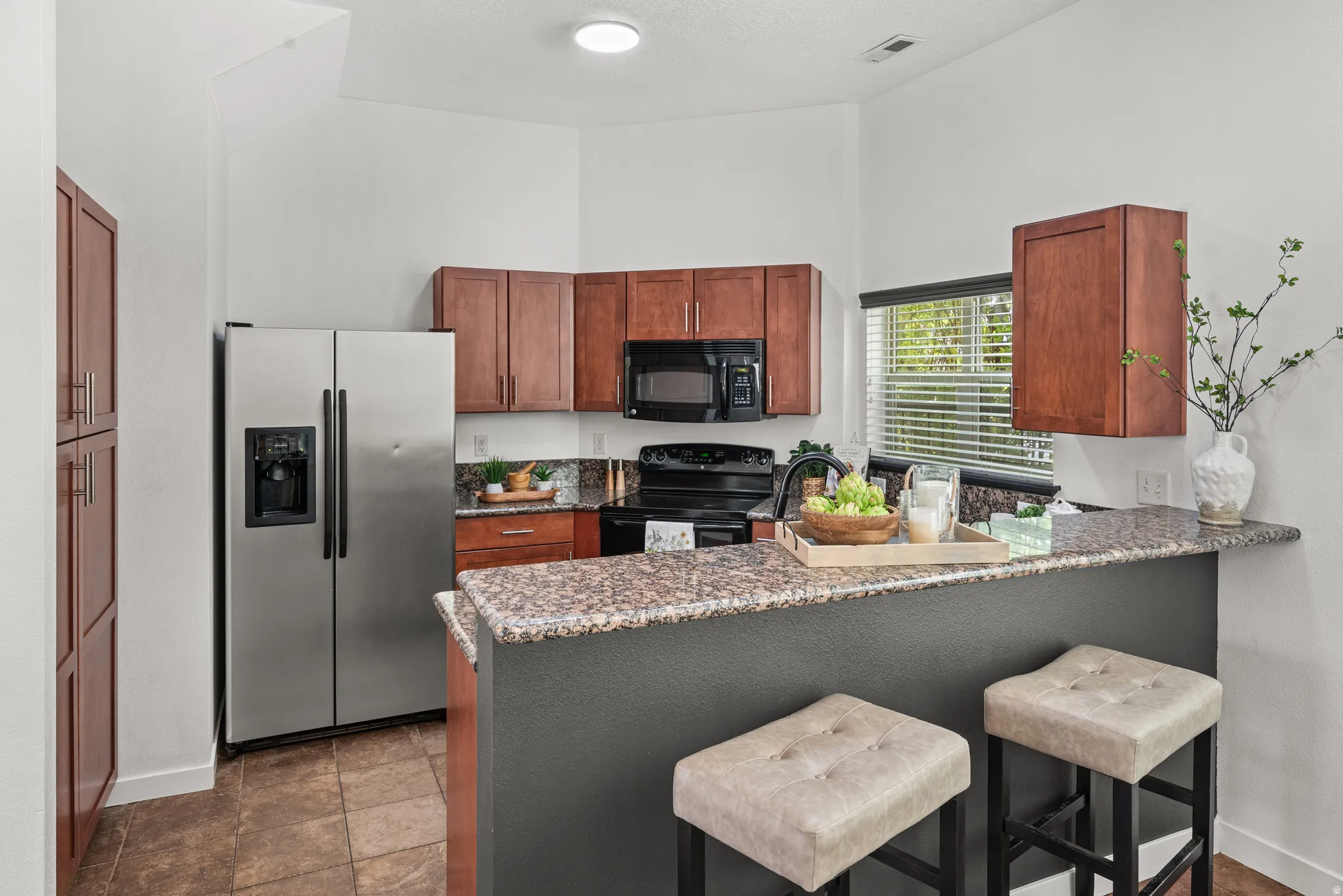 Kitchen featuring a kitchen breakfast bar, black appliances, a peninsula, dark stone counters, and a high ceiling
