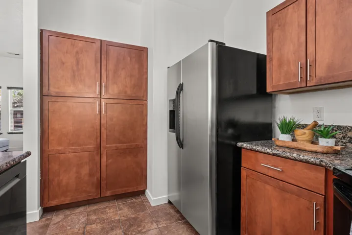 Kitchen featuring stainless steel appliances, wood finish cabinets, dark stone countertops, and dark stone finish floors