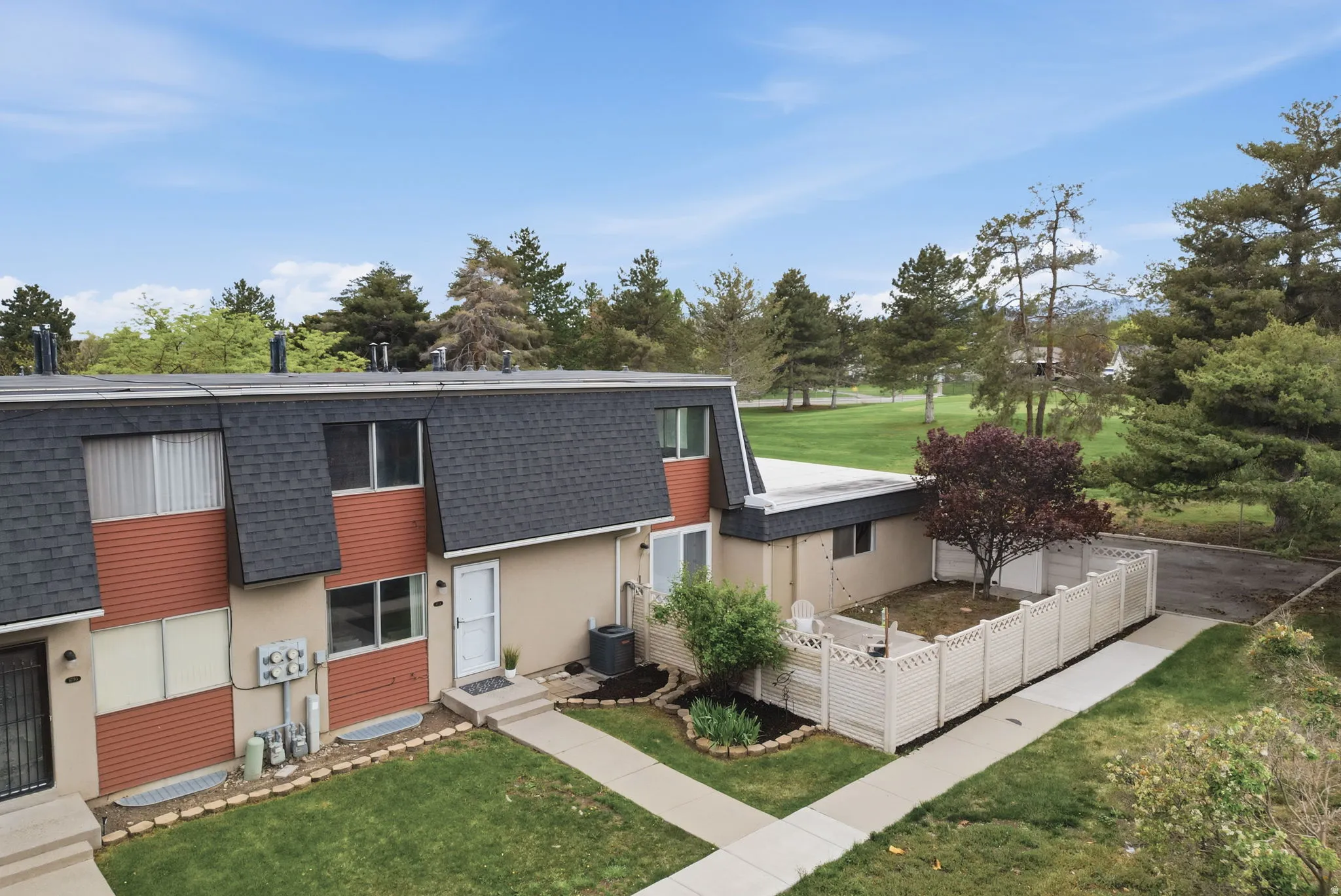 View of front of property featuring a shingled roof, mansard roof, stucco siding, entry steps, and view of wooded area