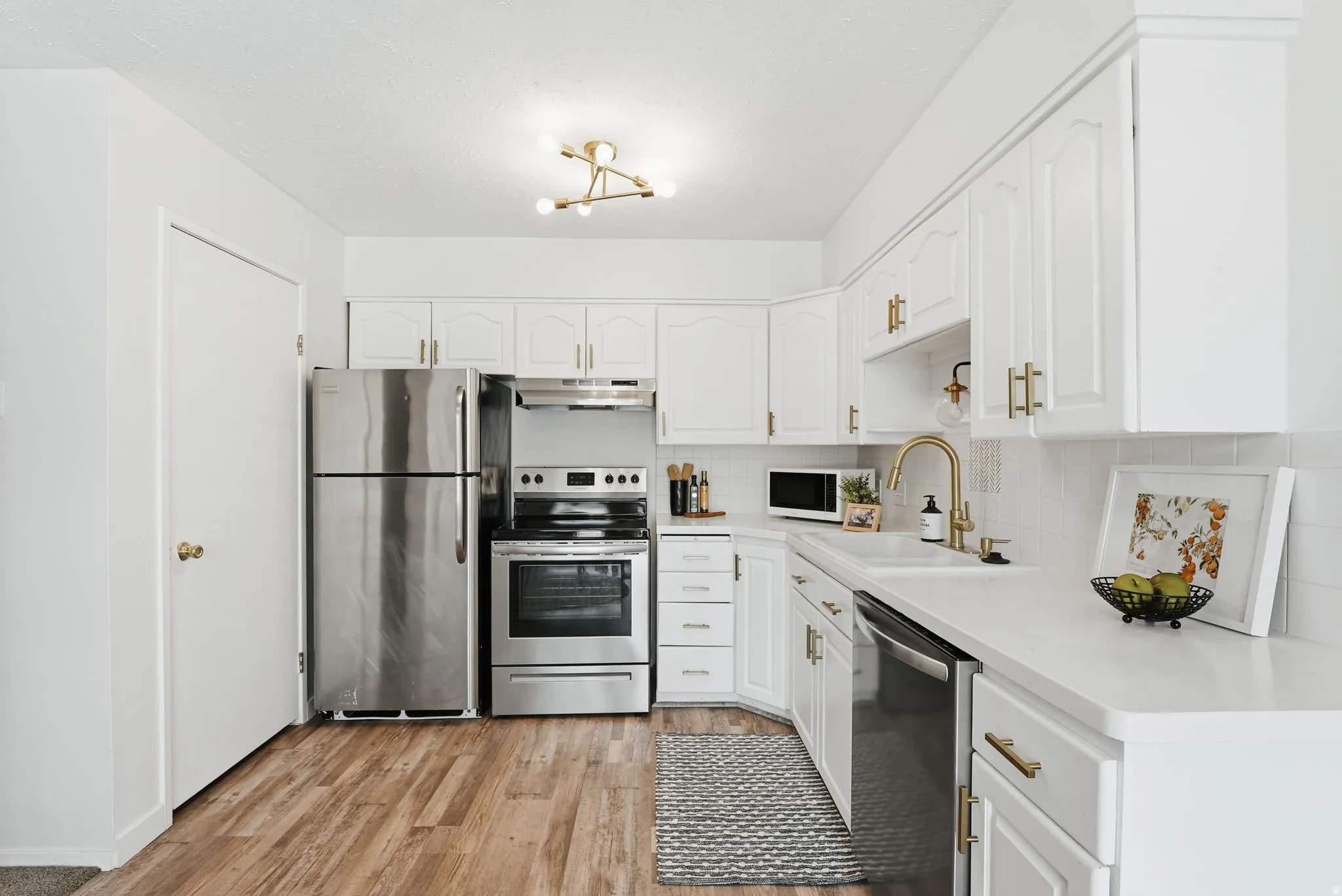 Kitchen with stainless steel appliances, light countertops, white cabinetry, and light wood-style floors
