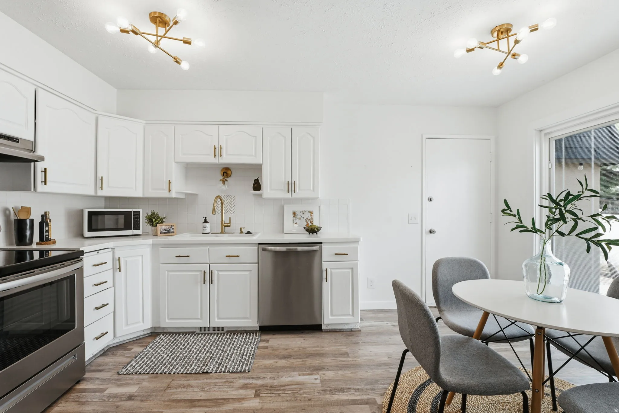 Kitchen featuring a chandelier, stainless steel appliances, white cabinetry, and light wood-type flooring