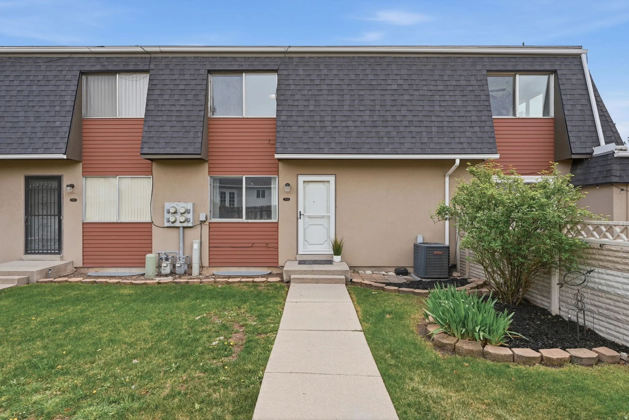 Contemporary home featuring a shingled roof, mansard roof, a front yard, and stucco siding