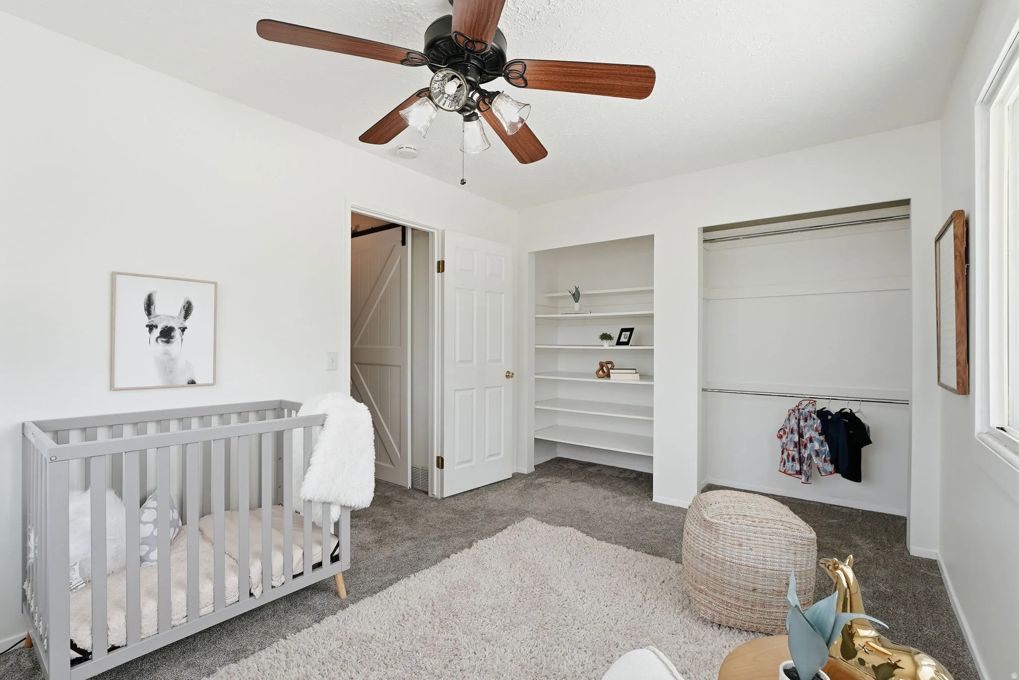 Bedroom with a crib, light colored carpet, ceiling fan, and multiple closets