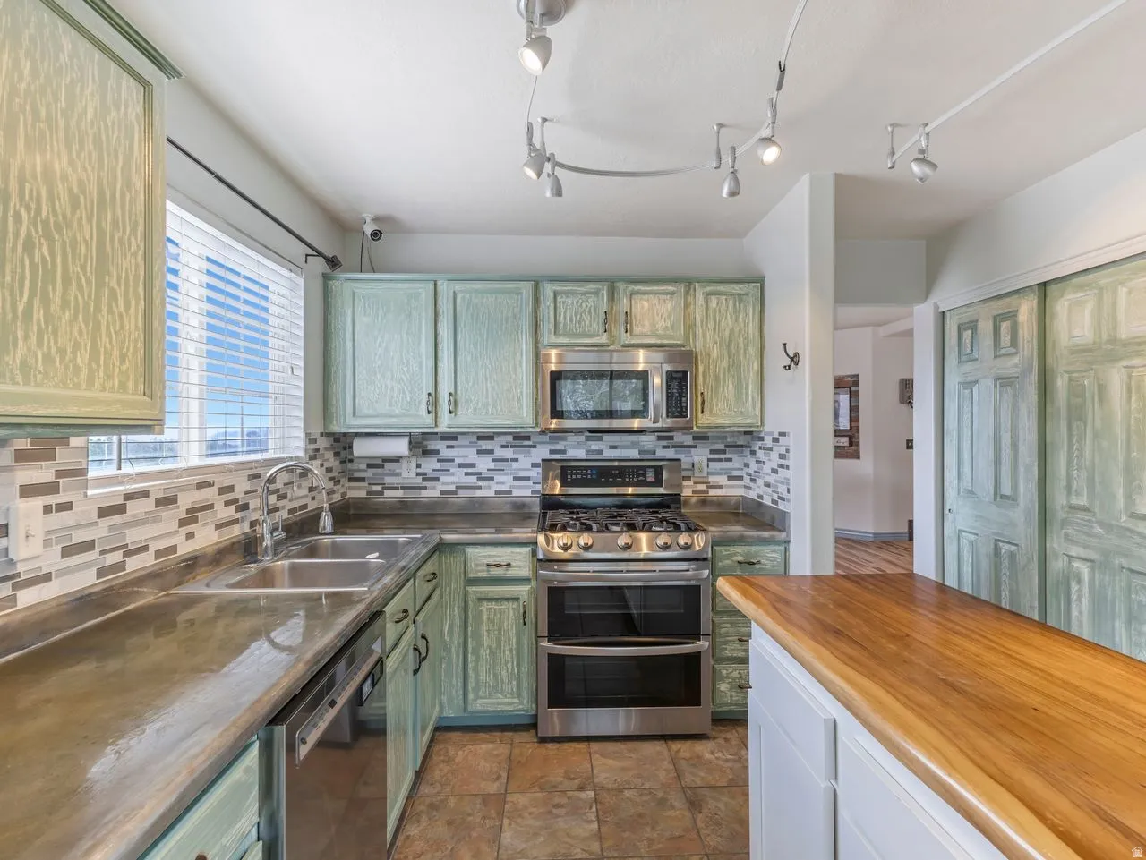Kitchen featuring stainless steel appliances, butcher block counters, green cabinets, dark stone finish flooring, and decorative backsplash