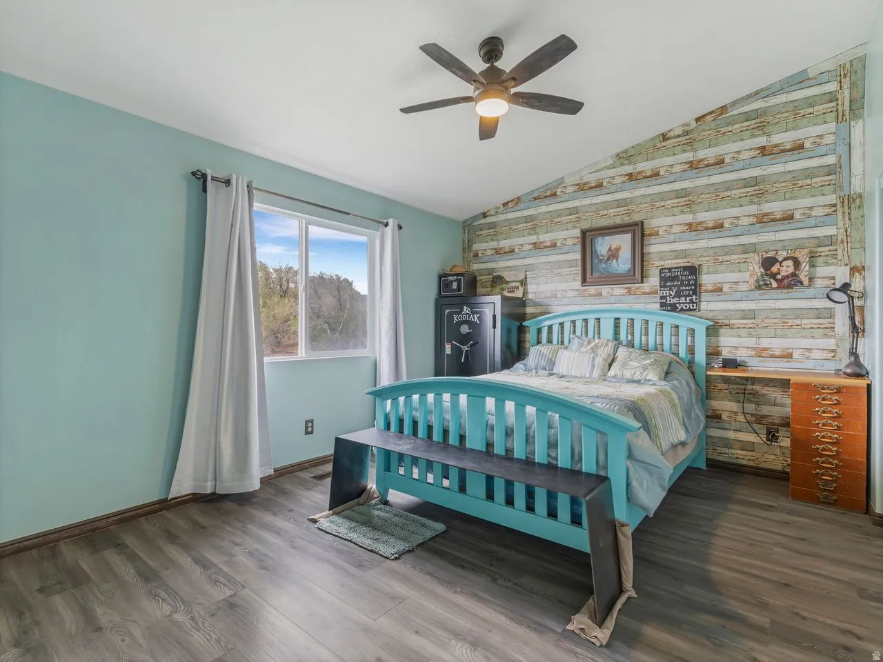 Bedroom featuring dark wood-style flooring, lofted ceiling, ceiling fan, and an accent wall