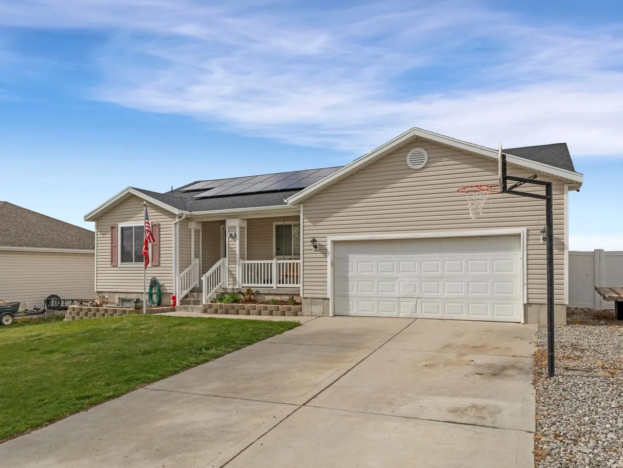 Ranch-style house featuring covered porch, concrete driveway, solar panels, a front lawn, and a garage