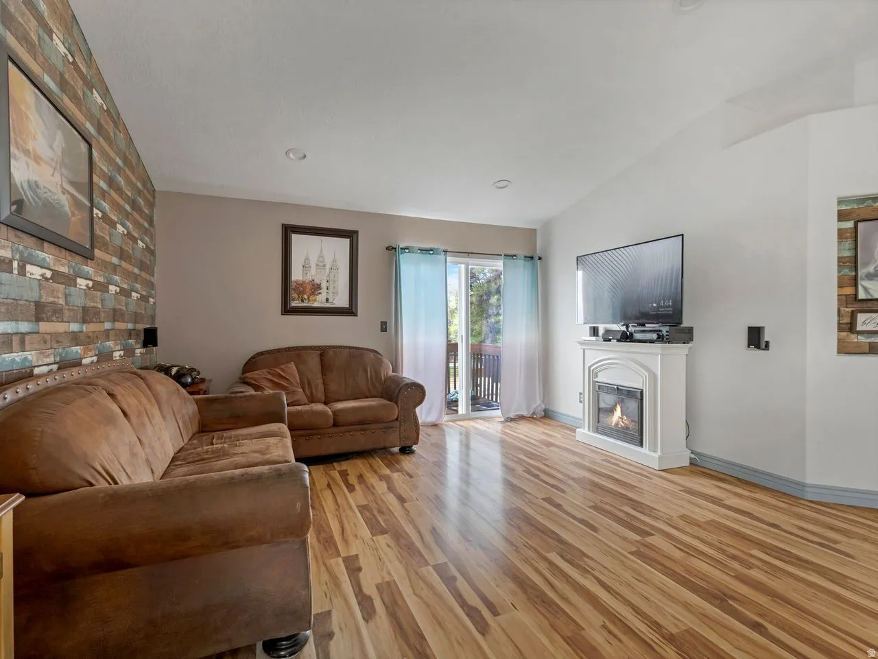 Living room with light wood-style flooring, vaulted ceiling, and a glass covered fireplace
