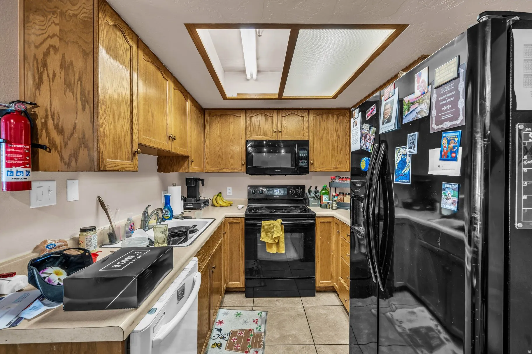 Kitchen featuring black appliances, light countertops, light tile patterned floors, and wood finish cabinetry