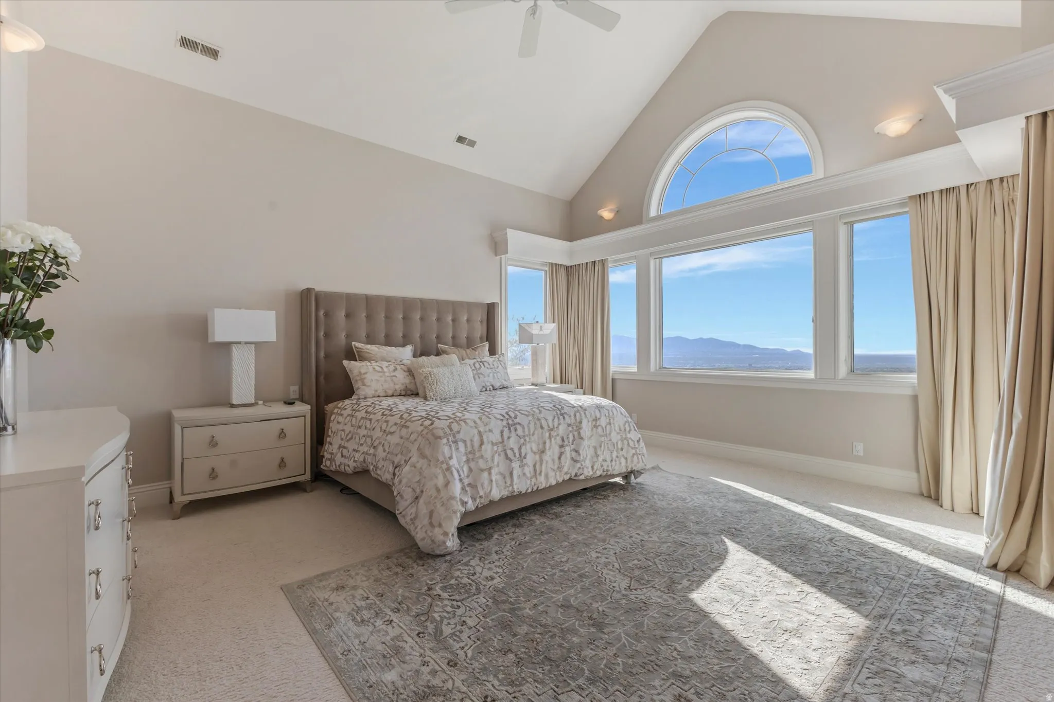 Bedroom with a mountain view, light colored carpet, multiple windows, a high ceiling, and a ceiling fan