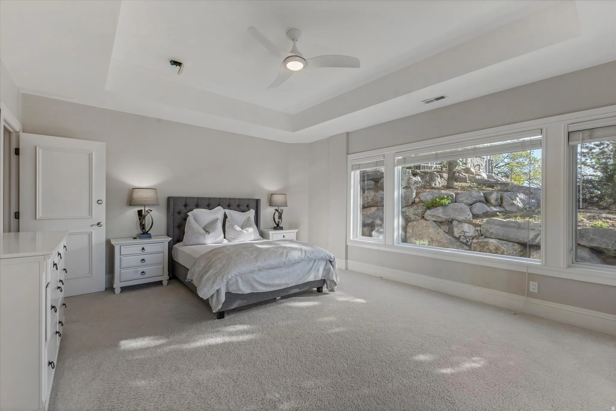 Bedroom with a tray ceiling, light carpet, and a ceiling fan
