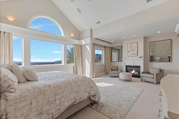 Bedroom with vaulted ceiling, a glass covered fireplace, and light carpet