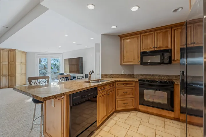Kitchen featuring a peninsula, a kitchen bar, black appliances, light stone countertops, and wood finish cabinets