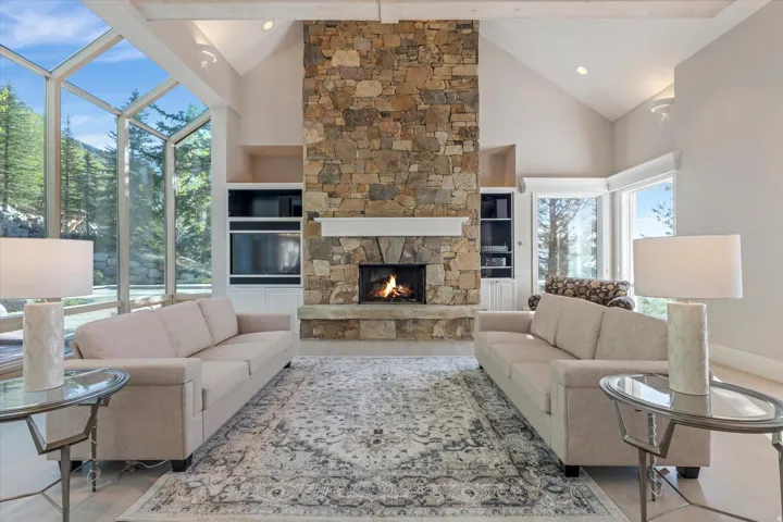 Living area featuring built in features, vaulted ceiling, a stone fireplace, a sunroom, and recessed lighting