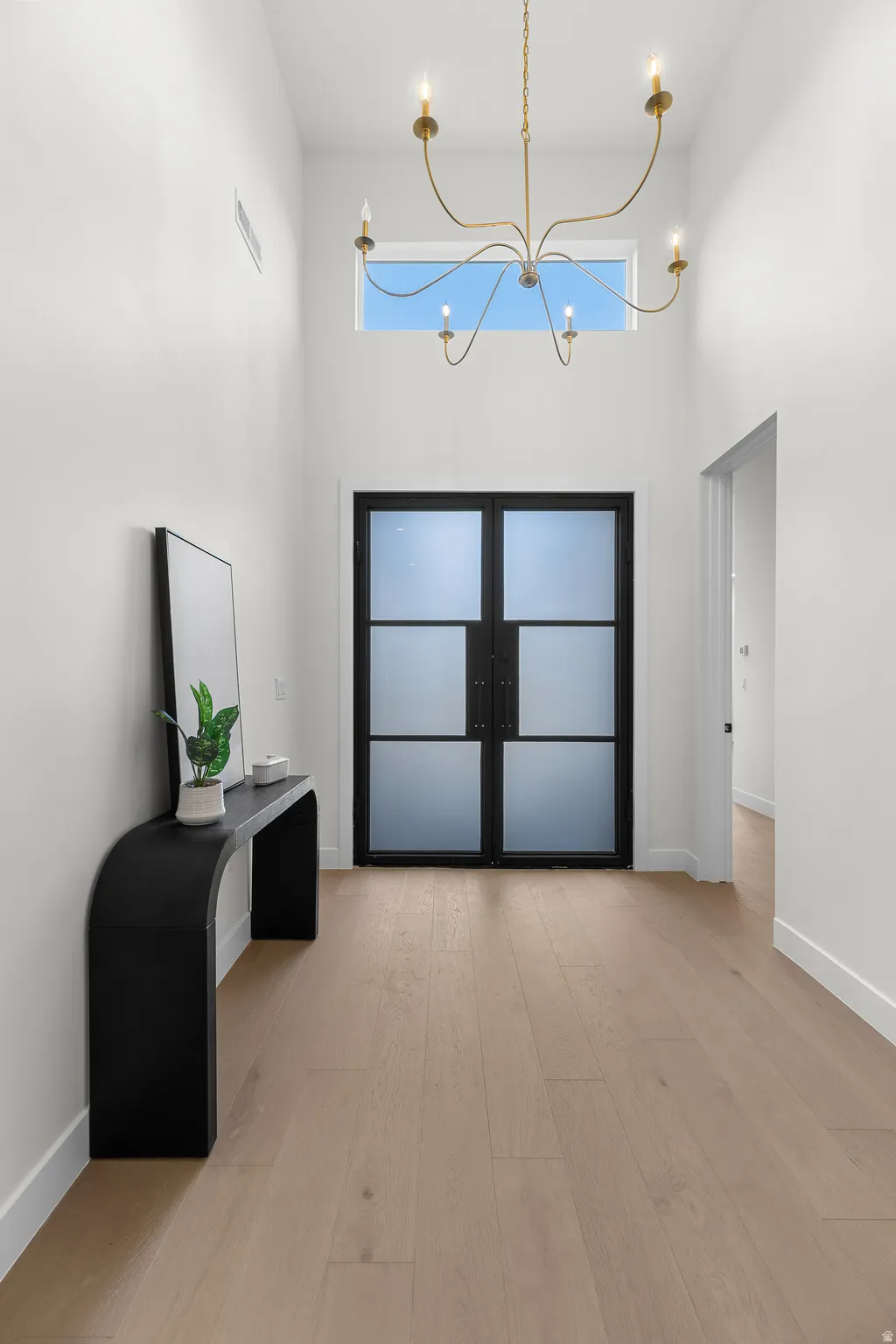 Foyer featuring a high ceiling, a chandelier, french doors, light wood-style floors, and healthy amount of natural light