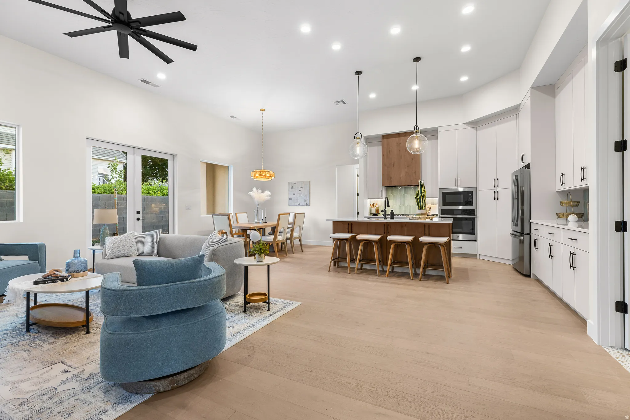 Living room with light wood finished floors, recessed lighting, french doors, a high ceiling, and ceiling fan