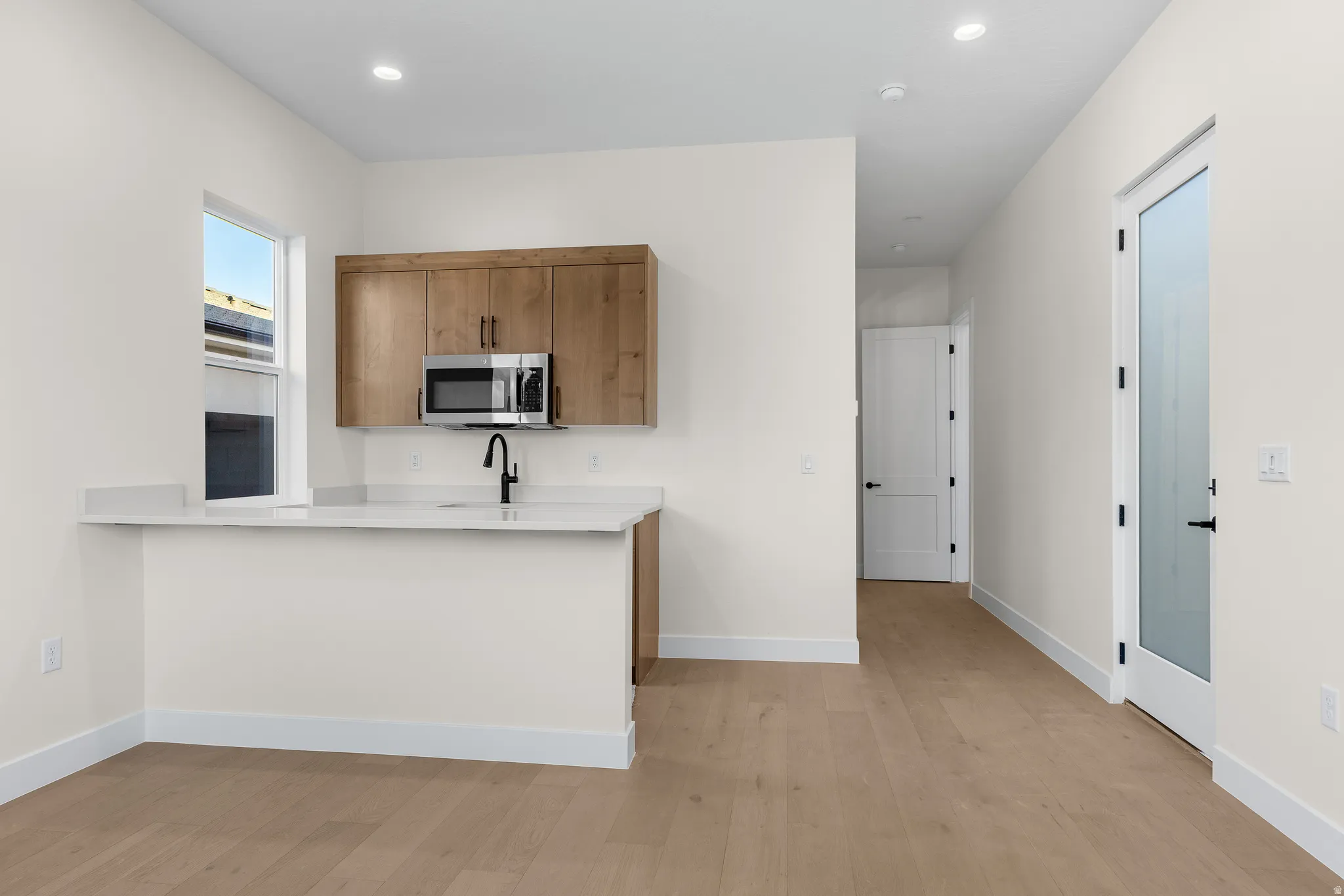 Kitchen with light wood-style floors, stainless steel microwave, a peninsula, wood finish cabinetry, and light stone countertops